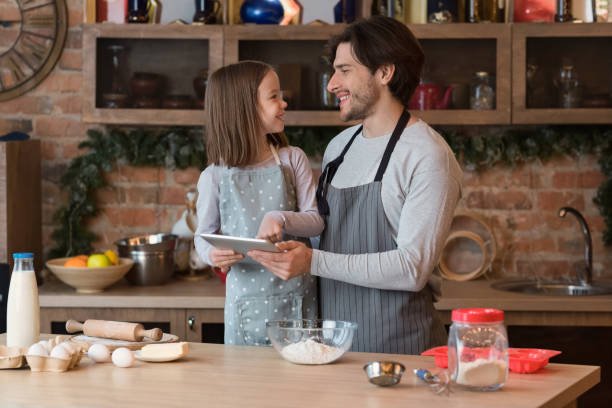 istock Little girl and her dad using digital tablet at kitchen, checking recipe 1250195983