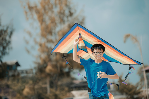 an asian chinese boy playing and flying kite at beach