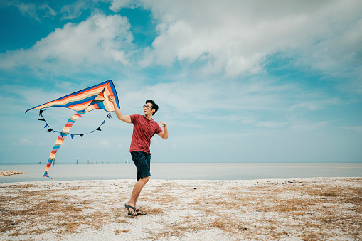 an asian chinese mid adult man playing and flying kite at beach