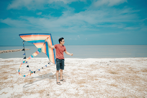 an asian chinese mid adult man playing and flying kite at beach