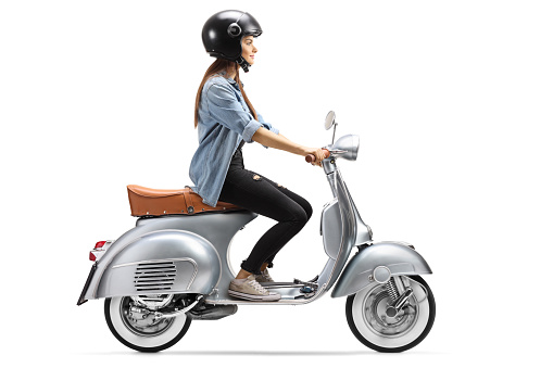 Full length profile shot of a young woman with a helmet riding a vintage scooter isolated on white background