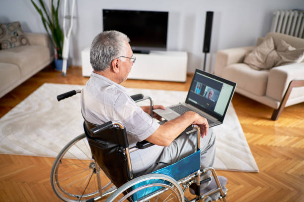 older man sitting in wheelchair, using laptop older man sitting in wheelchair, using laptop accessibility for persons with disabilities stock pictures, royalty-free photos & images