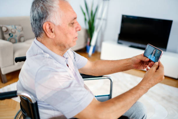 older man sitting in wheelchair, using mobile phone older man sitting in wheelchair, using mobile phone How Voice-Activated Technology Can Assist Parkinson's Disease Patients in Daily Activities stock pictures, royalty-free photos & images