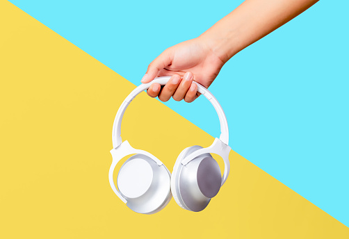 Female hands holding white headphones on blue and yellow background.