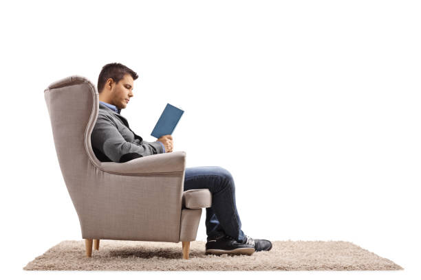 istock Young man sitting in an armchair and reading a book 1250205062