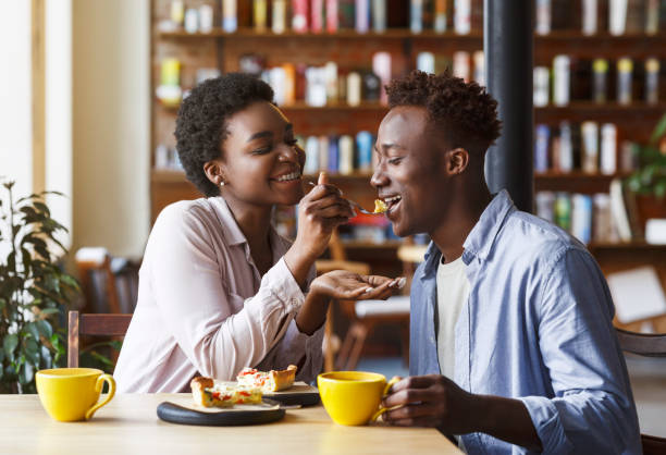 African American girl feeding tasty pie to her boyfriend in city cafe Cute love. African American girl feeding tasty pie to her boyfriend in city cafe savory food photos stock pictures, royalty-free photos & images