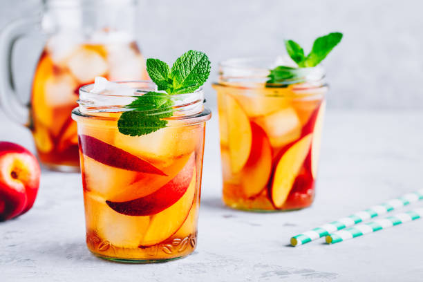 Homemade peach iced tea or lemonade with fresh mint and ice cubes in glass jar Homemade peach iced tea or lemonade with fresh mint and ice cubes in glass jar on gray stone background. iced tea stock pictures, royalty-free photos & images