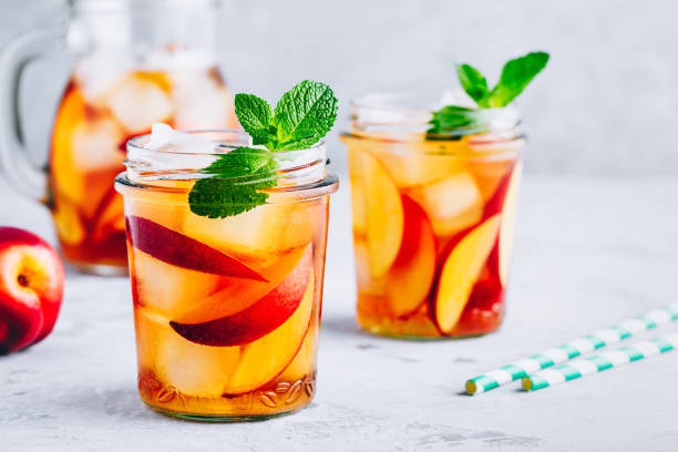 homemade peach iced tea or lemonade with fresh mint and ice cubes in glass jar - chá gelado imagens e fotografias de stock