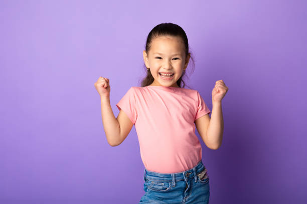 felice bambina asiatica che stringe pugni, fa gesto vincitore - child celebration cheering victory foto e immagini stock