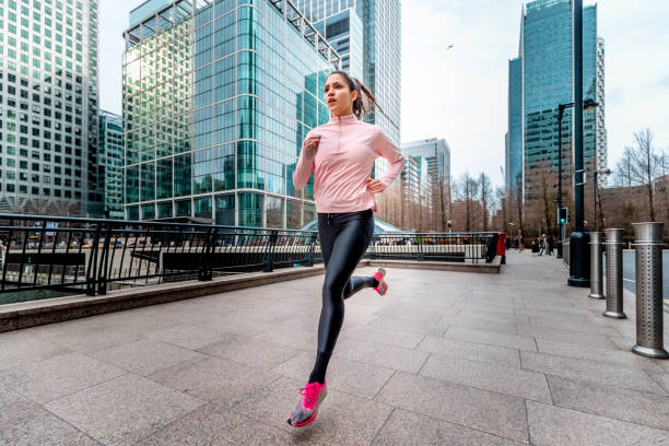 Woman jogging in London Full lenght of young sportswoman jogging in Canary Wharf district, unrecognizable commuters in background london docklands stock pictures, royalty-free photos & images