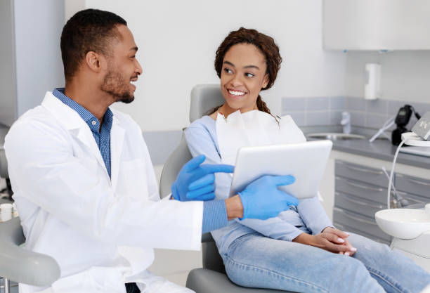 Cheery dentist showing patient clinic website on digital tablet Cheery african guy dentist showing woman patient his clinic website on digital tablet tablet pc and digital hospital tools stock pictures, royalty-free photos & images