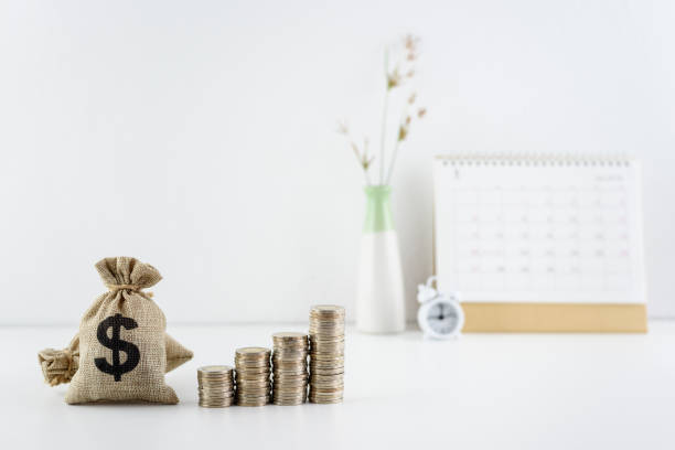 sacs en dollars, piles de pièces montantes, une horloge, calendrier renversé sur une table - timing is everything photos et images de collection