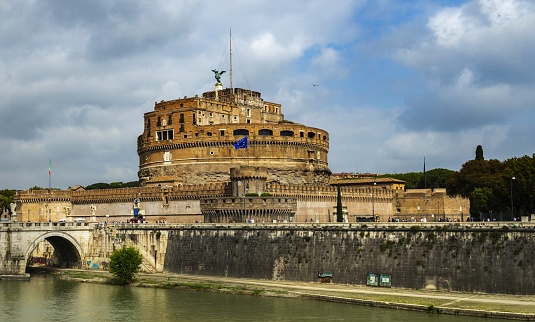 Rome, Italy, May 7, 2018: Castel Sant'Angelo with EU flag seen from the left bank of the Tiber River. The Castel was built between 135-139. It has been demolished, repaired and rebuilt several times over the years. Originally it was built by the Roman Emperor Hadrian as a family mausoleum, later served as a papal fortress connected by a tunnel in the walls with the Vatican, residences and prisons. It currently houses a museum dedicated to the history of the building and the city of Rome.