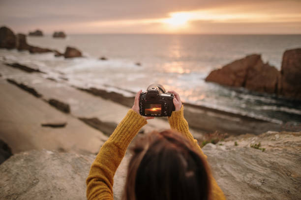 A young woman using a modern DSLR camera in a beautiful coast area at sunset