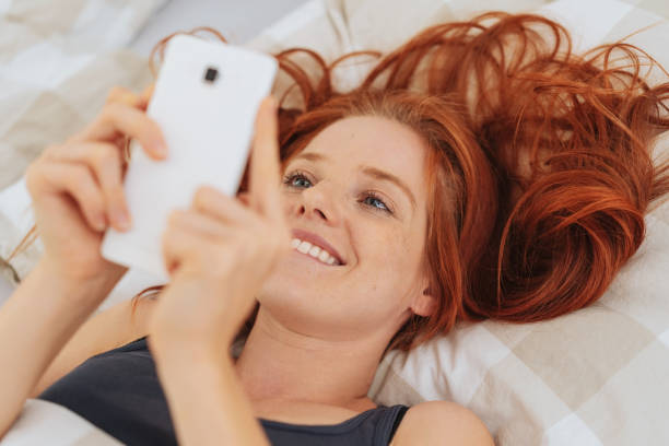 istock Young smiling woman using mobile phone in bed 1250229398