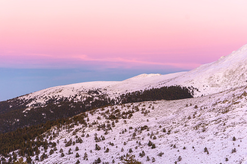 Sunset in mountains. Winter scenery. Beautiful pink and white sky, windy weather. Pink, purple and blue mild pastel colors