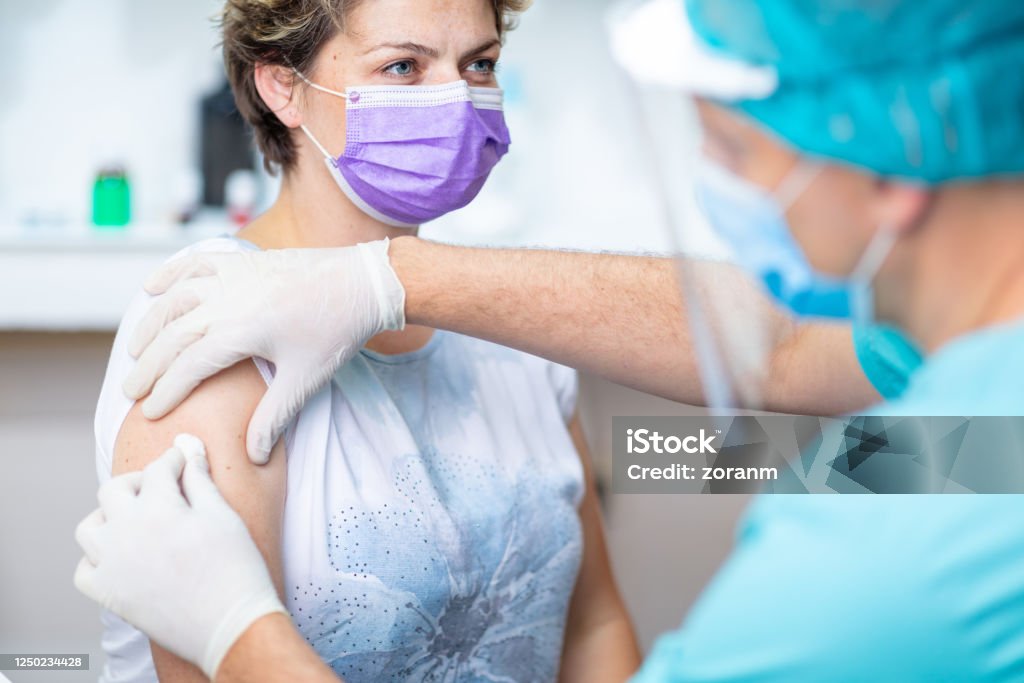 Female patient's arm disinfected with cotton pad for vaccination Female patient with protective face mask waiting for vaccination, doctor in surgical gloves disinfecting her arm Vaccination Stock Photo