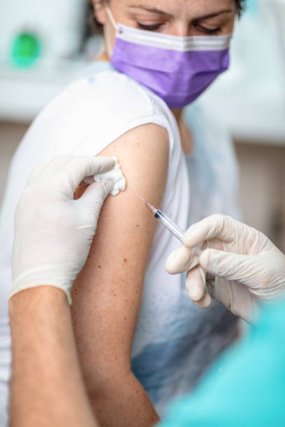 Female patient with protective mask looking at her arm after getting flu shot