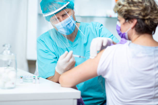 doctor in protective workwear giving flu shot and looking at female patient's arm - medicine cabinet medicine healthcare and medicine cabinet imagens e fotografias de stock