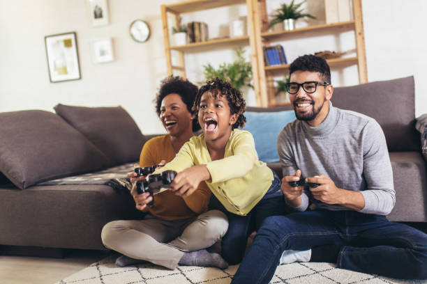 African American family at home sitting in sofa couch and playing console video games together African American family at home sitting in sofa couch and playing console video games together family at home stock pictures, royalty-free photos & images