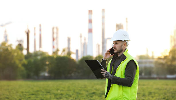 istock Young engineer with smartphone standing outdoors by oil refinery. Copy space. 1250240787