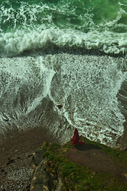 High angle view of mysterious woman wearing red at the coastline on the edge of the sea