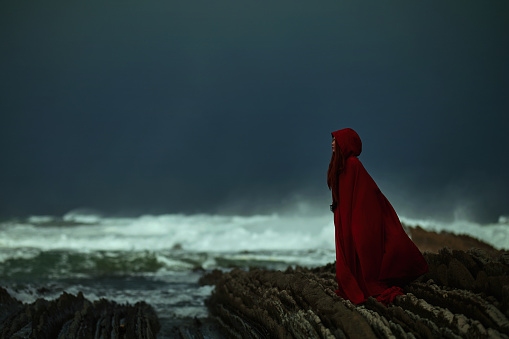 Profile view of mysterious woman wearing red cape on the coastline