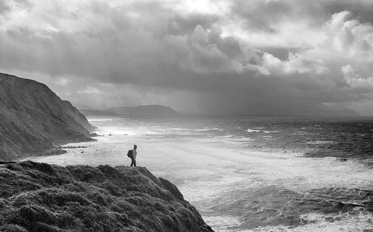 Monochrome shot of woman standing on the edge of water on the cliff, feeling free and happy