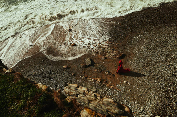 High angle view of mysterious woman wearing red at the coastline on the edge of the sea
