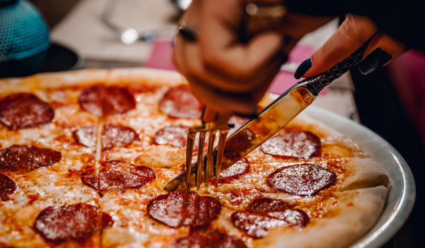 istock woman hands with knife and fork cutting pepperoni pizza on table in cafe 1250244613