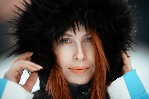 Redhead woman with blue eyes wearing winter  clothes and black fur posing, looking at the camera seriously; winter time