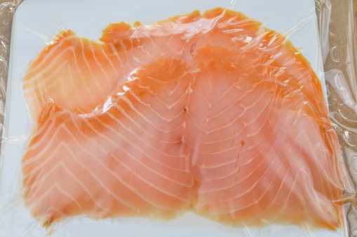 Smoked salmon slices in package on a wooden cutting board close up