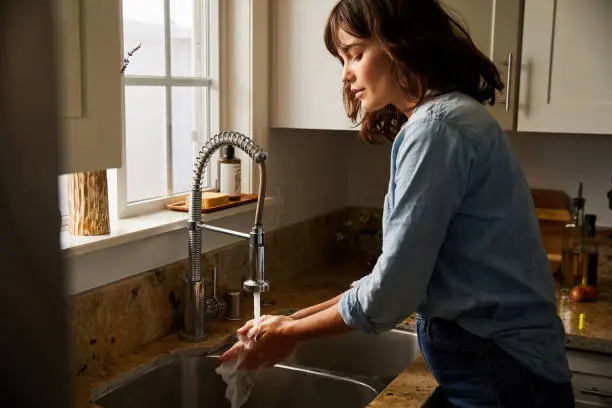 Photo of Young woman washing her hands under running water in her sink