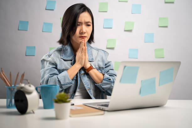 asiatische frau hält hände im gebet lesen nachrichten auf laptop im innenministerium. die wfh. arbeiten sie von zu hause aus. prävention coronavirus covid-19 konzept. - pleading women business sadness stock-fotos und bilder