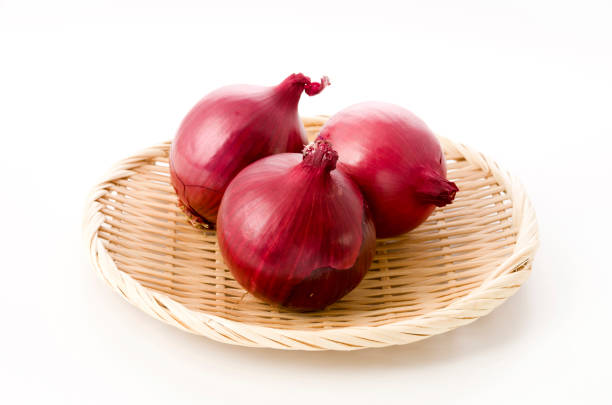 Fresh red onion in bamboo colander on white background