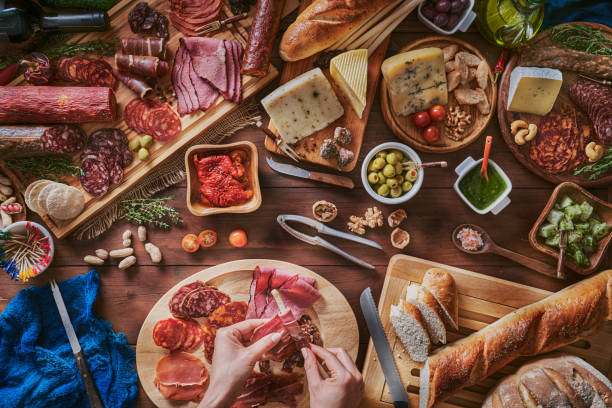 istock Female hands preparing snacks and appetizers in a set full of assorted Cured ham and cheese on rustic wood 1250252121
