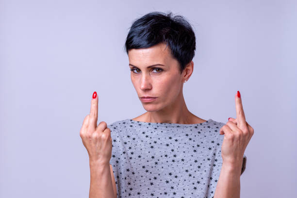 Attractive woman making a middle finger gesture Attractive woman making a derogatory middle finger gesture with both hands pointing to herself while looking thoughtfully at the camera over a grey background derogatory stock pictures, royalty-free photos & images