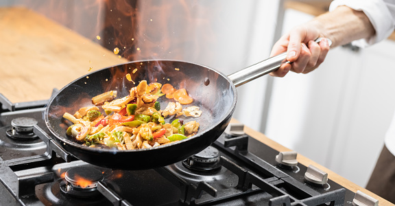 Unrecognizable chef throwing veggies and meet in the wok.