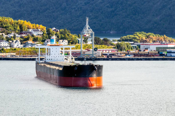 Empty bulk iron ore carrier at anchor in Arctic Circle harbour Empty bulk iron ore carrier at anchor in Narvik harbour (Norway's Arctic Circle). Waiting to load with gantry crane, iron ore train, residential houses, Fjord & mountains in background. All ID, names, logos removed. bulk carrier stock pictures, royalty-free photos & images