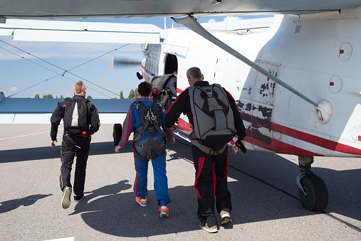 Skydiving instructor leads a woman to the plane. The videographer shoots on vieo how they go.