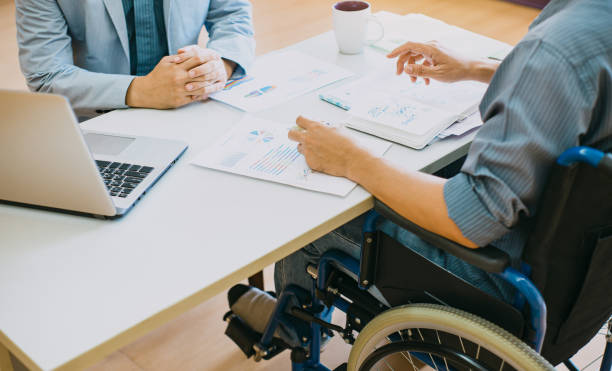 Man on wheelchair with his boss. After car accident and rehabilitation, a businessman can return to work again. The company which employing disable people will receive tax deductions benefits. physical injury stock pictures, royalty-free photos & images