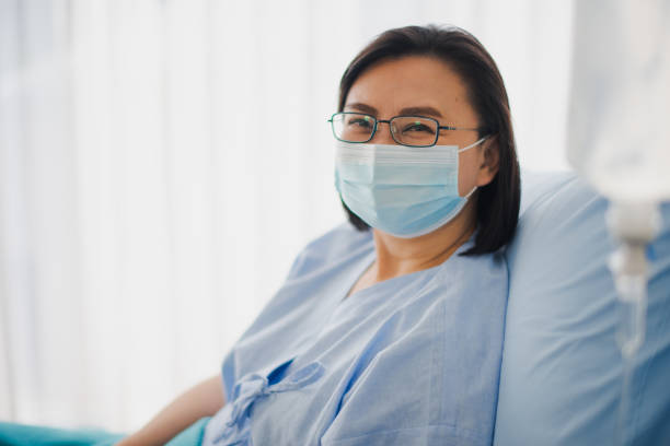 高齢のアジアの患者女性は、病院のベッドに座ってマスクの下で幸せに微笑み、落ちる。医学およびヘルスケアの安全な概念。 - visit hospital patient senior adult ストックフォトと画像