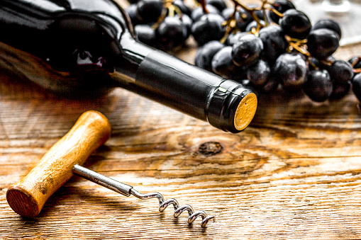 Glass of red wine and bottle with corkscrew and grape on wooden desk background