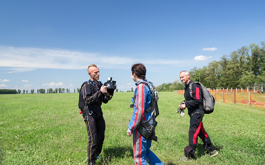 A woman walks with skydiving instructor and videographer along the airfield to the plane. The videographer is shooting a video.