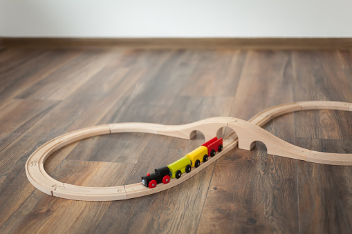 Wooden toy train on railroad with wooden bridge. Clean laminated floor