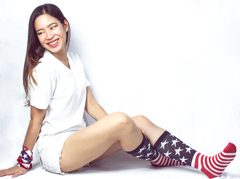 Portrait of beautiful woman wearing clothes decorated by american flag and sitting on white background for celebrating independence day on 4th of July. Symbol and Fashion concept.