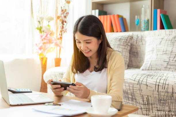 istock Asian girl playing online games application or chatting text message with friend by using smart phone smiley face at house during break time of working at home that make her get relax, fun, happy 1250279387