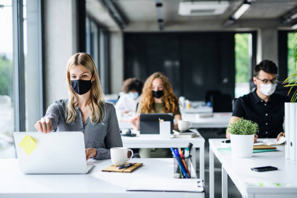 Young people with face masks back at work or school in office after lockdown. Young people with face masks back at work in office after coronavirus quarantine and lockdown. lockdown business stock pictures, royalty-free photos & images