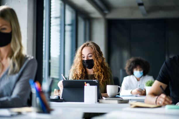 istock Young people with face masks back at work or school in office after lockdown. 1250279786