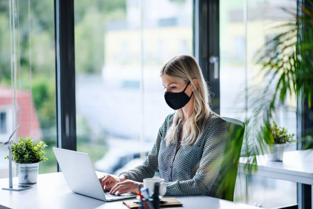 istock Young woman with face mask back at work in office after lockdown, using laptop. 1250279822